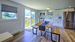 Eine moderne Küche mit Holztisch, weißen Schränken, Edelstahlgeräten und einer Glastür zum Balkon.