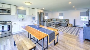 Eine moderne Küche mit Einbauherd, Mikrowelle und Kühlschrank. Ein Essbereich mit Holztisch und Bänken ist vorhanden. Im Wohnbereich steht ein graues Sofa und ein Fernseher auf einem Schrank.