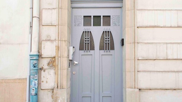 Un edificio con una entrada grande y arqueada, el número '5' sobre la puerta, y un buzón a la izquierda.