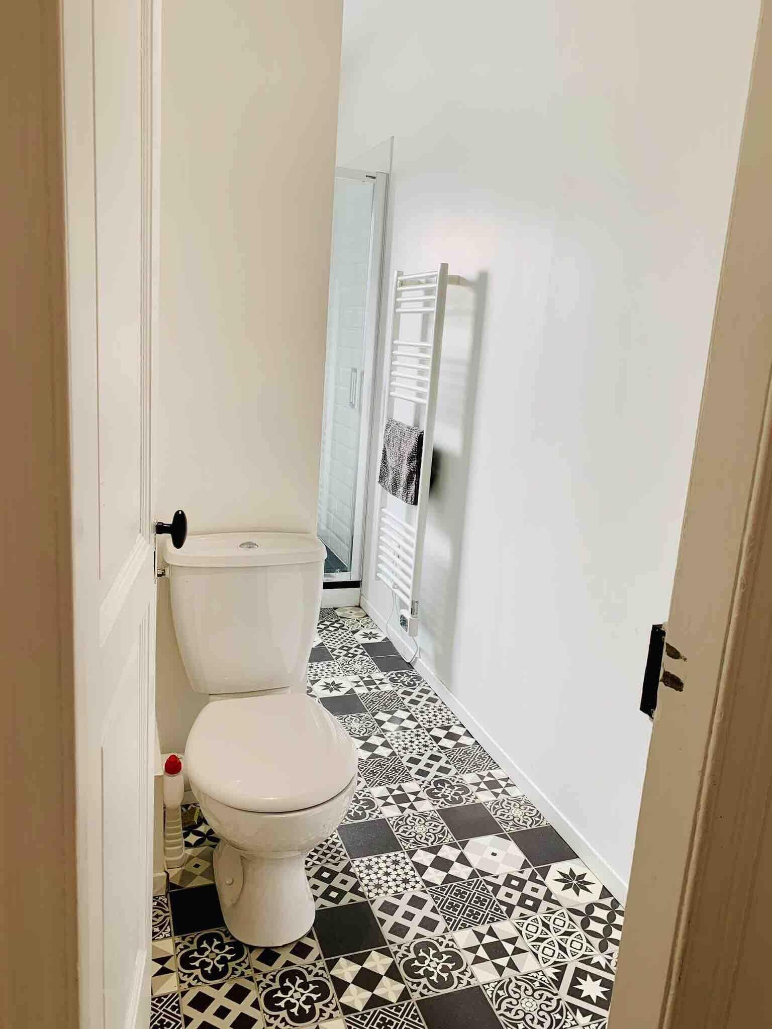 Um banheiro pequeno com vaso sanitário branco, ladrilhos no chão com padrão e um porta-toalhas.