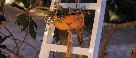 A white wooden ladder with lights, a hanging planter with greenery, and a tree trunk.