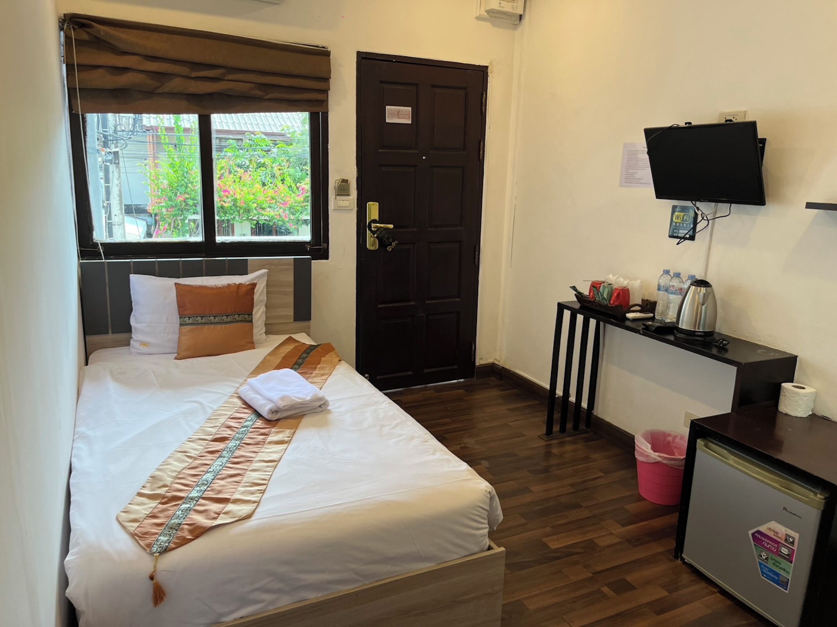 A hotel room with a bed, a small desk, a television, and a refrigerator.