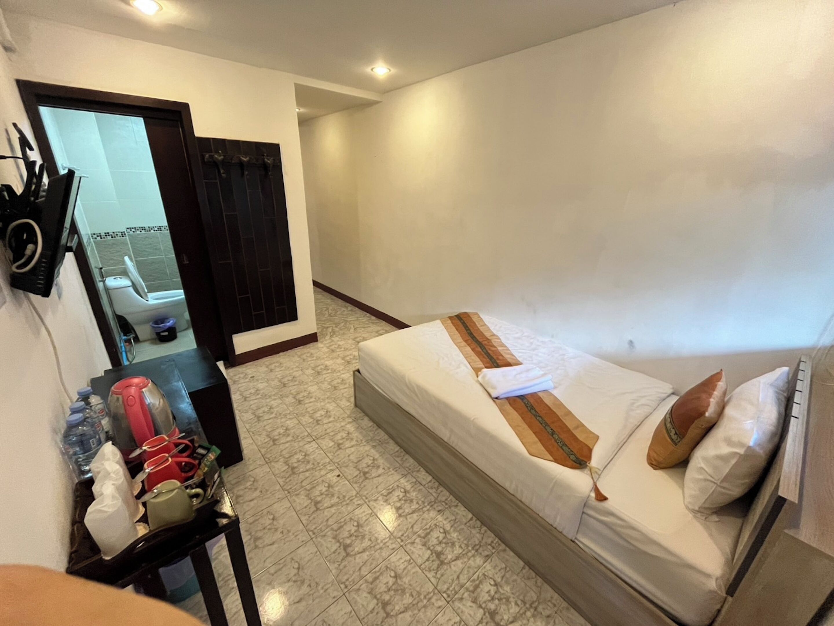 A hotel room with a bed, a small table with toiletries, a mirror, and a view of the bathroom.