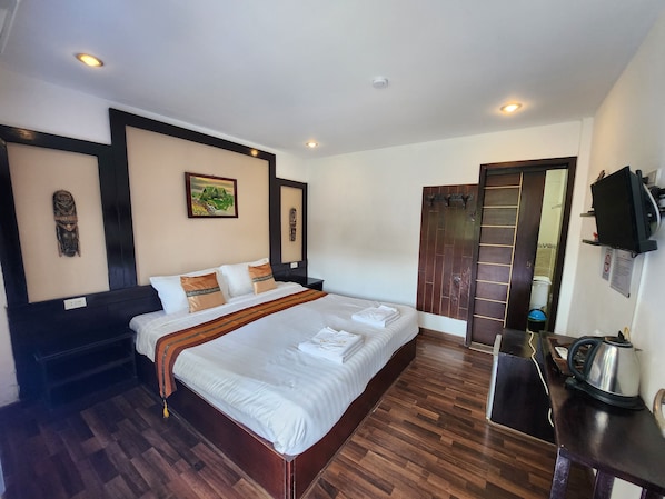 A hotel room with a large bed, wooden flooring, a painting on the wall, and a television mounted on the wall. - Pai Residence Hotel (Chiang Mai)