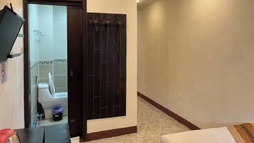 A hotel room with a large mirror, a dark wooden door, a white toilet, and a small trash bin.