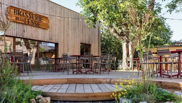 An outdoor seating area with wooden tables and chairs, a wooden deck, and a sign reading "BRASSERIE DE LA LESSE". - A peaceful night's sleep at La Chapelle (Rochefort)