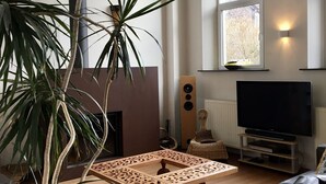 A living room with a large plant, a wooden coffee table, a black sofa, a television, and a window with a view of trees. - A peaceful night's sleep at La Chapelle (Rochefort)