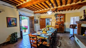 Un coin repas avec un plafond en bois, une longue table dressée pour six personnes et une cuisine dotée de meubles en bois et d’un four encastré.