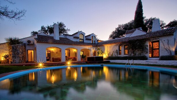 Vista de una piscina junto a una casa con muros de piedra y puertas de arco.