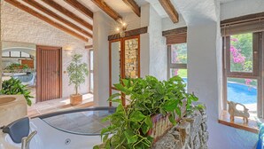 Un área de spa con una bañera de hidromasaje acristalada, vigas de madera, paredes de piedra y plantas en macetas.