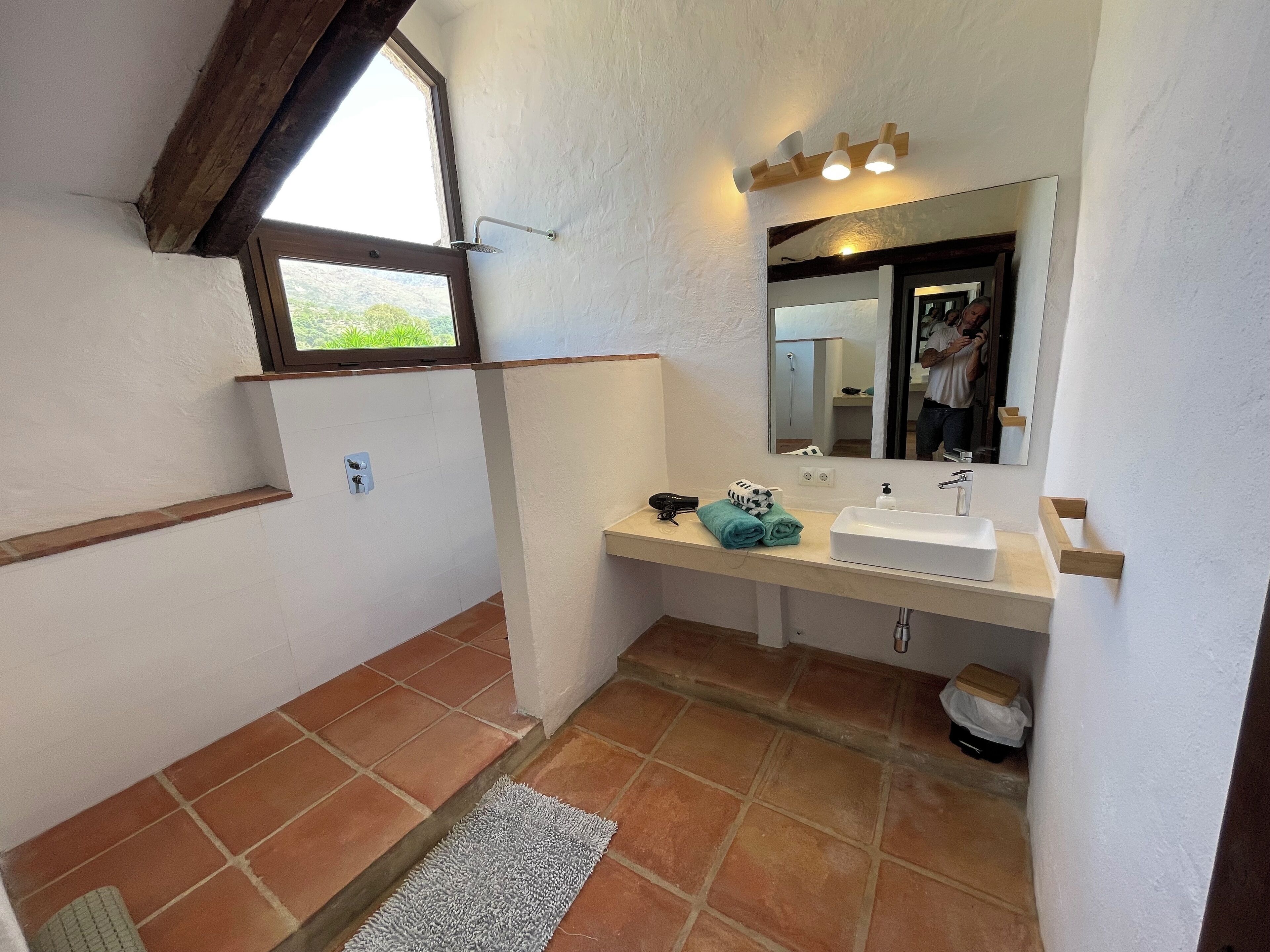 A bathroom with a white sink, a mirror, a shower, and a window.