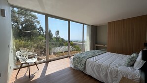 Un dormitorio moderno con un ventanal grande, una cama, una silla y suelo de madera.