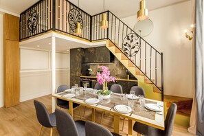 A dining area with a glass table set for six, a kitchen in the background, and a staircase with a black railing.