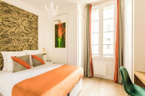 Ein Hotelzimmer mit Bett, einer Kandelaber, einem Fenster mit Vorhängen und einer Wand mit einem Blattmuster.