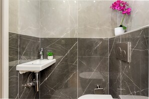 Ein modernes Badezimmer mit einem мраморной раковине, einer kleinen Pflanze und einem Orchideenstrauß.