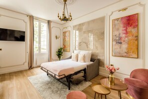 A modern bedroom with a bed, a sofa, a TV, and artwork on the walls.