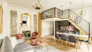 A spacious living room with a modern sofa, a dining area with a wooden table and chairs, a staircase with a decorative railing, and a kitchen area visible through an open door. - Merveil - Luxury Suite -ChampsElysees- Florentin I (Paris)
