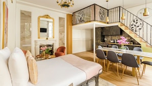 A spacious living area with a large bed, a dining table with chairs, a kitchen, and a staircase with a railing. - Merveil - Luxury Suite -ChampsElysees- Florentin I (Paris)