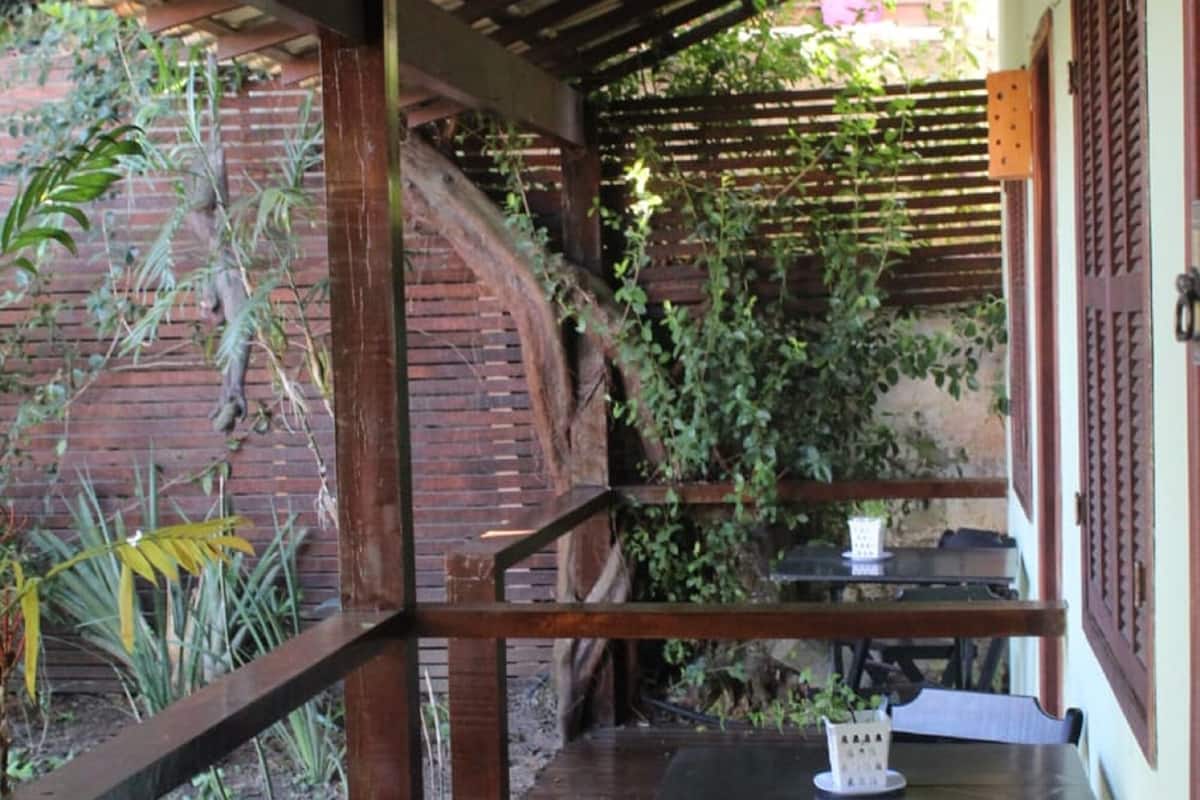 A wooden deck with a table and chairs, surrounded by greenery and a brick wall.
