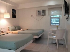 A small, modern room with two single beds, a desk, a chair, a TV, and a window with blinds. - Wanderlust Bed and Breakfast Puerto Princesa (Puerto Princesa)