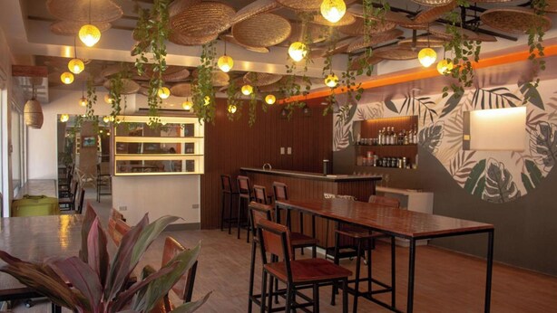 A restaurant with wooden tables and chairs, hanging plants, and a wall mural. - Wanderlust Bed and Breakfast Puerto Princesa (Puerto Princesa)