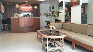 A reception area with a wooden reception desk, a glass-top table, a sofa, and a potted plant. - Wanderlust Bed and Breakfast Puerto Princesa (Puerto Princesa)