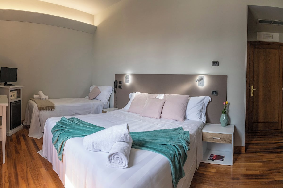 Ein Hotelzimmer mit zwei Betten, einem Schreibtisch mit Computer, einem Nachttisch mit einer Vase und Holzboden.