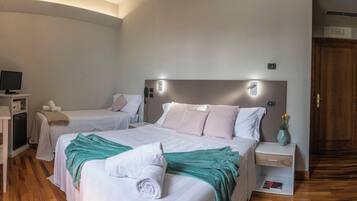 A hotel room with two beds, a desk with a computer, a bedside table with a vase, and a wooden floor.
