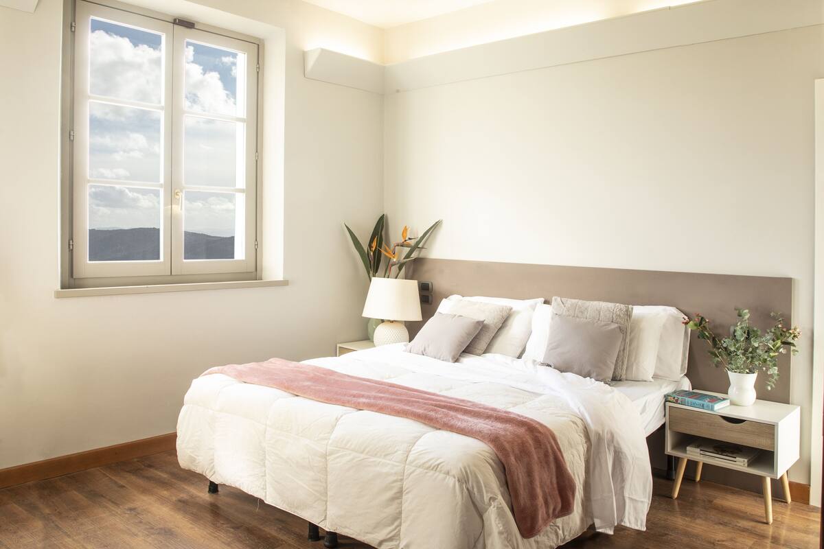 Ein Schlafzimmer mit Bett, Nachttisch, Lampe und einem Fenster mit Blick.