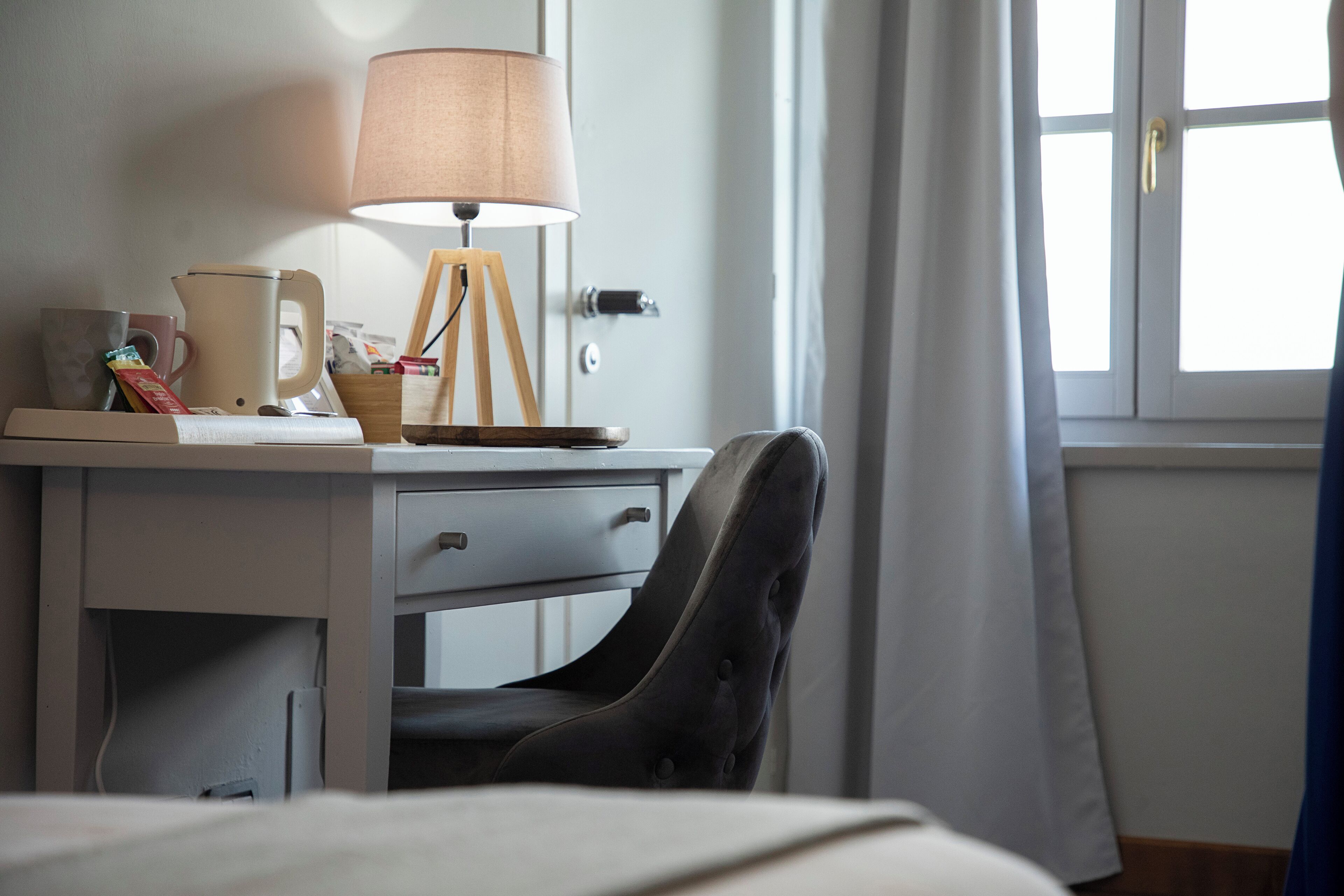 A hotel room with a desk, a lamp, a chair, and a window with curtains.