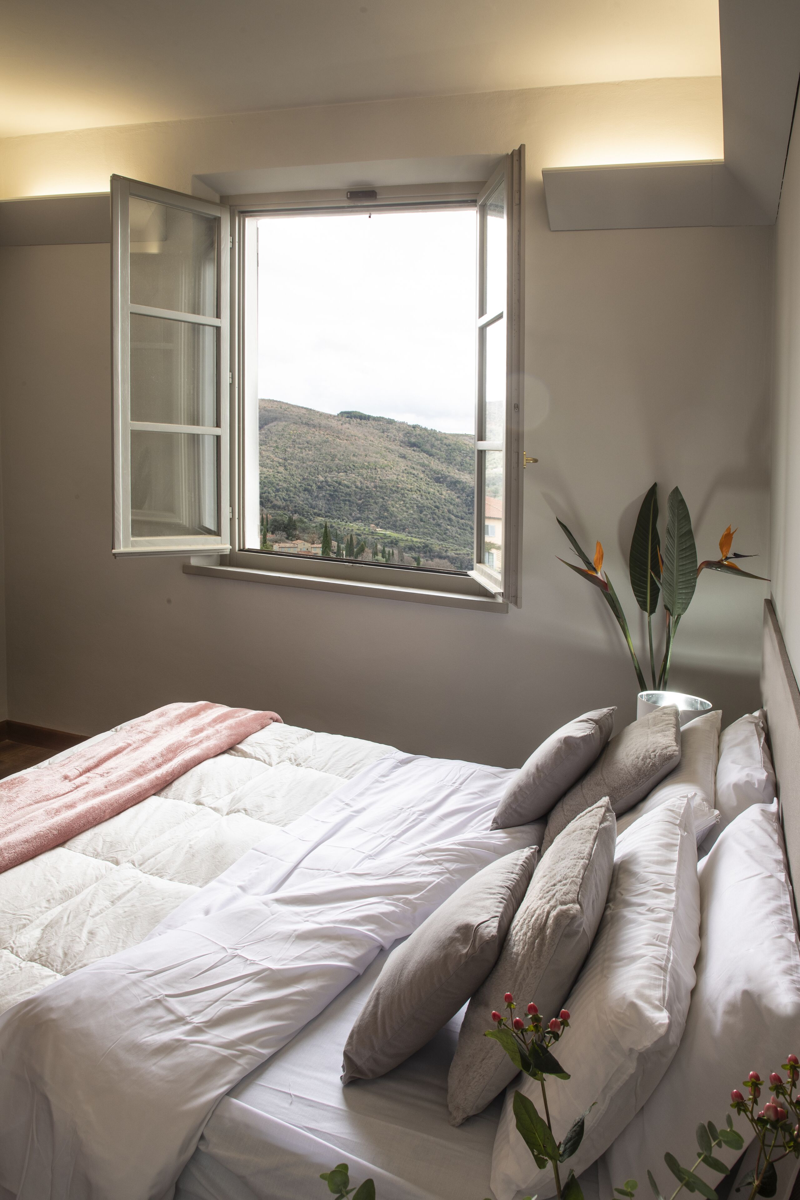 Une chambre à coucher avec un lit, des oreillers, une fenêtre donnant sur un paysage dégagé et une plante.