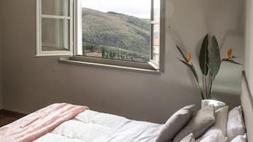 Une chambre à coucher avec un lit, des oreillers, une fenêtre donnant sur un paysage dégagé et une plante.