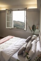 Un dormitorio con cama, almohadas, ventana con vistas abiertas y una planta.