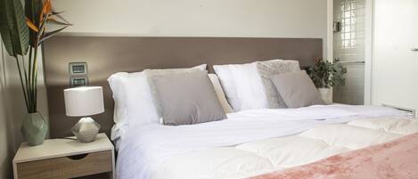 A neatly made bed with a white and pink blanket, a bedside lamp, and a plant on the nightstand.