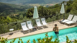 Zona de piscina con sillones reclinables y sombrillas, con vistas a un paisaje pintoresco.