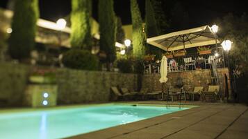 A nighttime outdoor pool area with a stone wall, lounge chairs, and a canopy.
