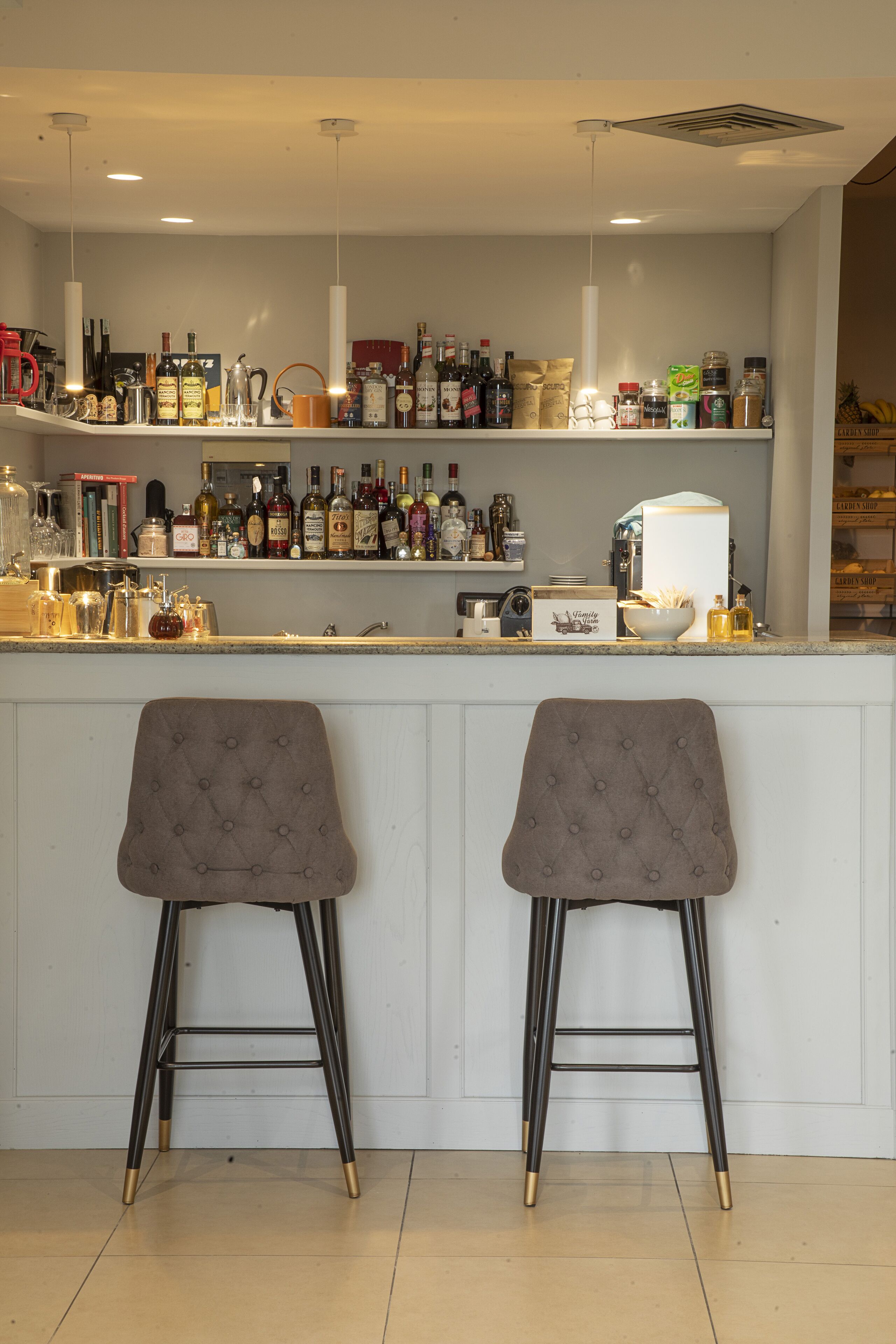 Un coin bar avec deux tabourets, une variété de bouteilles et une machine à café.