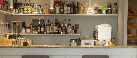 A bar area with two stools, a variety of bottles, and a coffee machine.