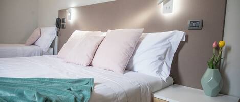 Habitación de hotel con una cama grande, una mesita de noche con un jarrón de flores y un escritorio pequeño con un cajón.