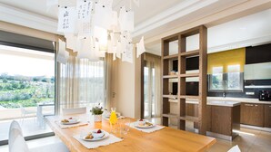A modern dining area with a wooden table set for breakfast, a kitchen with wooden cabinets, and a view of greenery outside. - Deluxe Villa Ianthos - Outdoor Hot Tub & Kids Pool (Rethymno)