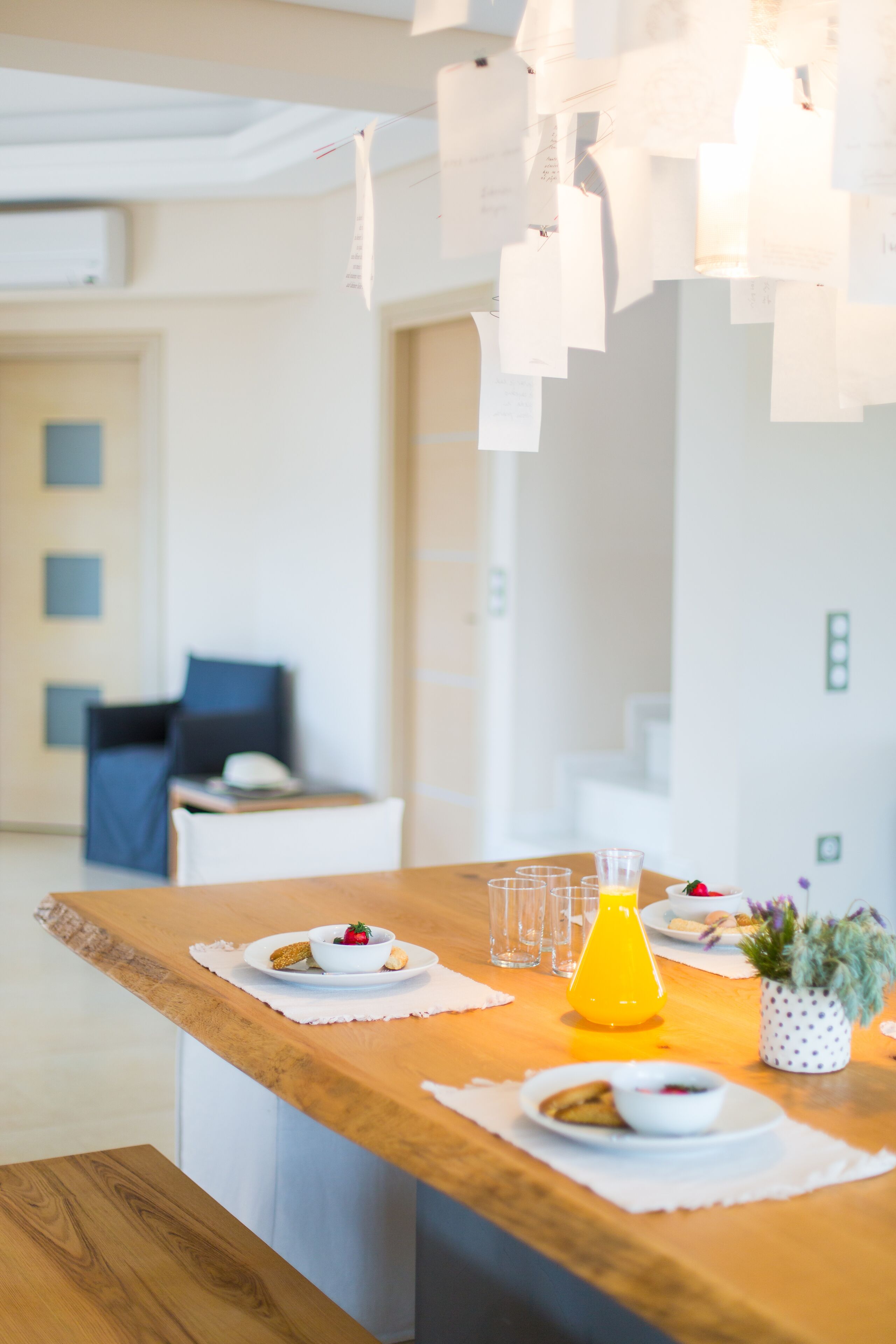 A modern dining area with a wooden table set for breakfast, including plates, glasses, and a yellow vase with flowers.