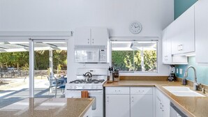A modern kitchen with white cabinets, a gas stove, a microwave, and a dishwasher. There is a window providing a view of the outdoors. - Alexander in the Sun - Mid‑Century Pet‑Friendly Oasis: Pool, Spa & Mountains (Palm Springs)