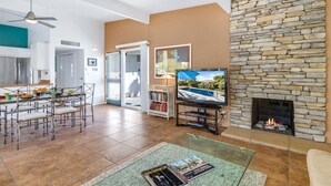 A spacious living area with a stone fireplace, a television, and a dining area with chairs and a table. - Alexander in the Sun - Mid‑Century Pet‑Friendly Oasis: Pool, Spa & Mountains (Palm Springs)