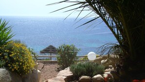 Un jardin agrémenté d’un belvédère, de rochers et de fleurs, qui offre une vue sur la plage.