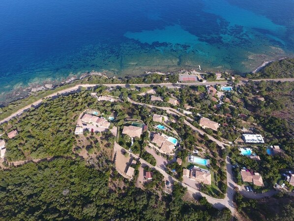 An aerial view of a coastal residential area with houses, roads, and a clear blue sea. - Stunning 2/4-person apartment in a villa with a pool and panoramic ocean views (Conca)