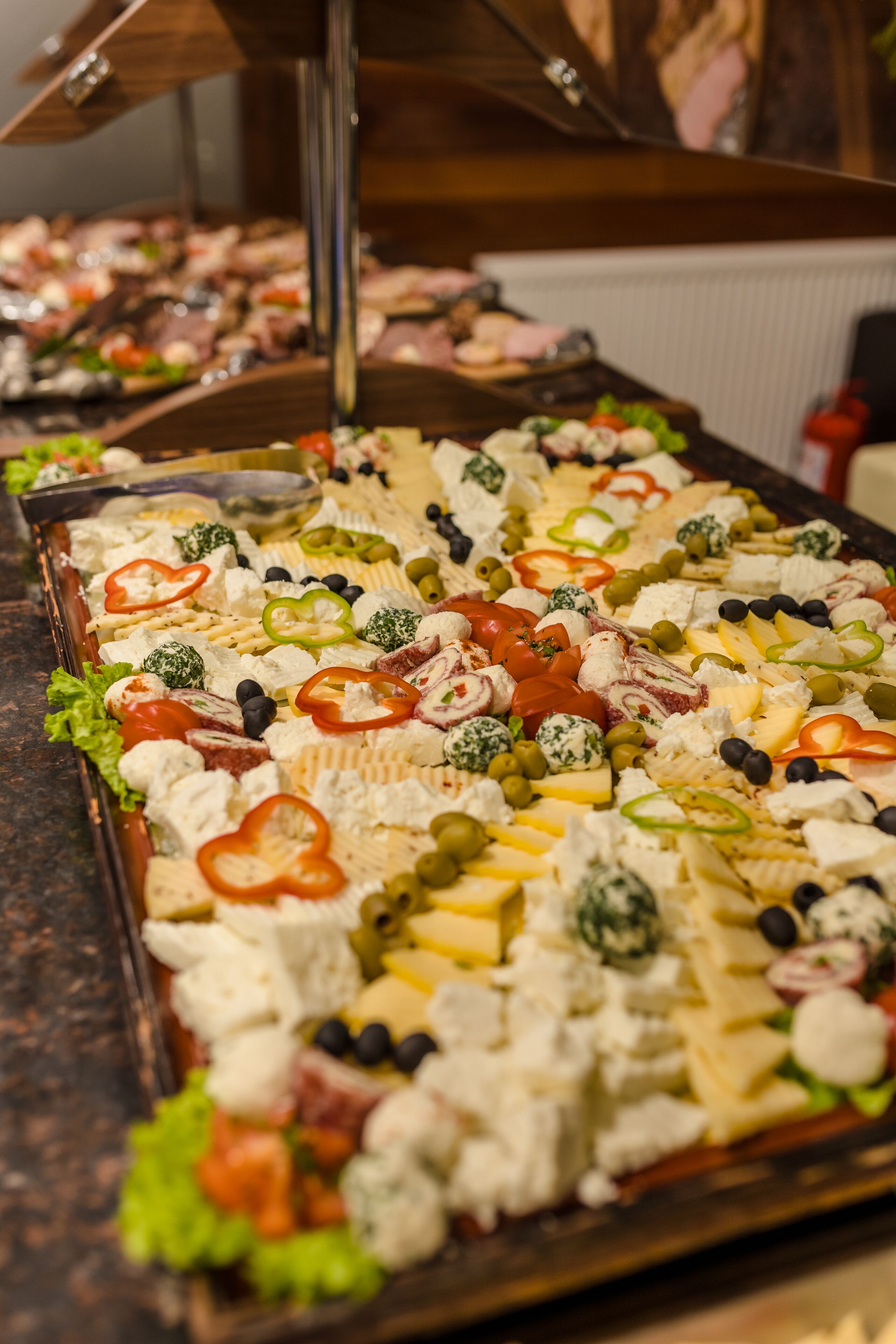 A buffet with various cheeses, olives, and vegetables.