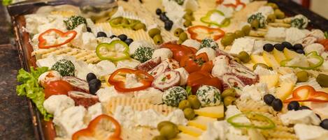A buffet with various cheeses, olives, and vegetables.