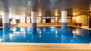 An indoor swimming pool with clear blue water, tiled walls, and a modern ceiling design. - Hotel Cindrel (Sibiu)