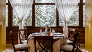 A dining table set for four with a view of snow-covered trees through large windows. - Hotel Cindrel (Sibiu)