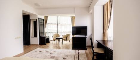Quarto de hotel com cama, escrivaninha, cadeira, televisão e janela com cortinas.